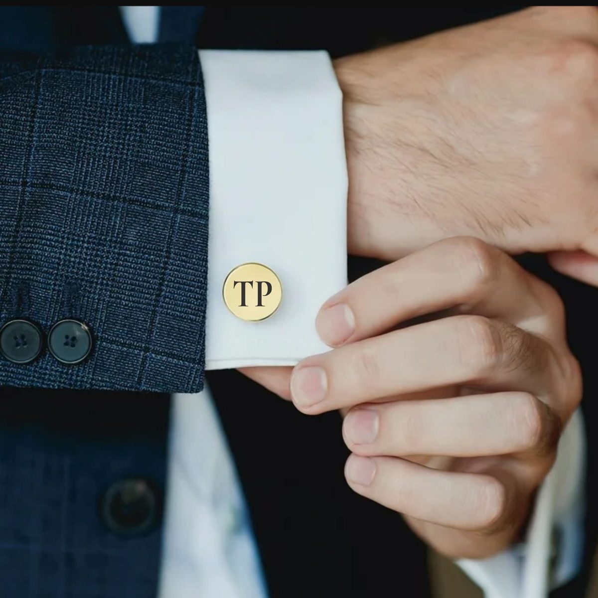 Auksinė sąsaga su inicialais „TP“ prisegta prie marškinių rankogalio